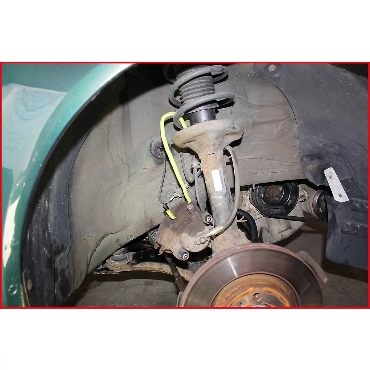 Nahaufnahme der Radaufhängung eines Autos mit Federung, Bremsscheibe und gelber Leitung.